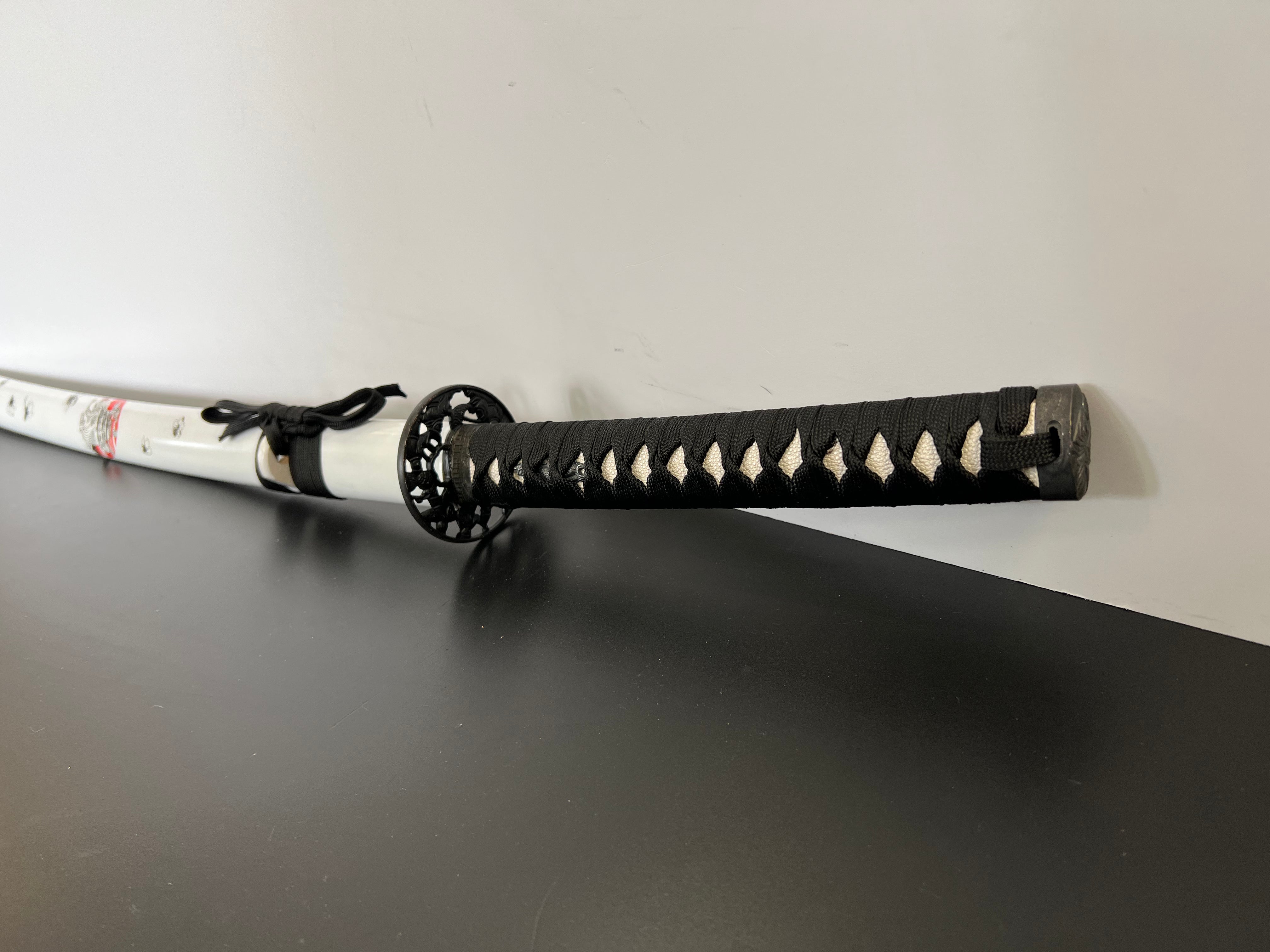 Katana mit weißen Kirschblütenmuster. Das Samuraischwert hat Kirschblüten Verzierungen auf der ganzen Saya (Schwertscheide) und die Kirschblüte ist eines der wichtigsten Symbole in Japan, sie steht für Schönheit, Aufbruch und Vergänglichkeit und zeigt sich in der schönsten Jahreszeit, dem Frühling. Die Kirschblüte wird im Japanischen Sakura genannt und wird von vielen Japanern aufgrund ihrer Schönheit gepflanzt. Zudem spiegelt die Kombination aus Katana und Kirschblüte die Japanische sehr gut wieder.